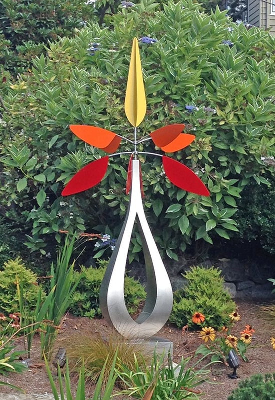 shaped stainless sculpture kinetic placed in a garden with flowers