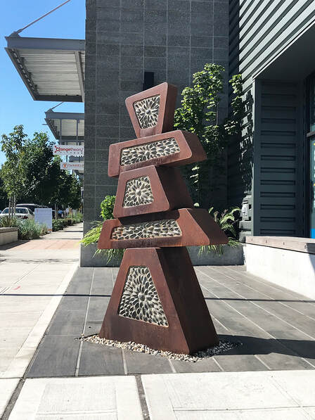 corten steel and stone inlay sculpture that looks like a carin or stacked rocks